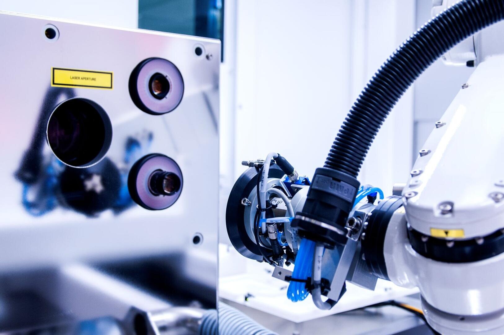 Close-up of an advanced robotic machine in a laboratory environment with metallic components, cabling, a laser label and a mechanical arm with precision instruments.