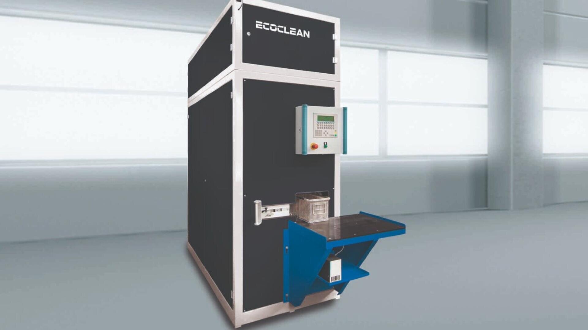 A large, black and white industrial machine labeled Ecoclean sits in a bright, modern room. The machine features a control panel and a blue tray extending from its side.