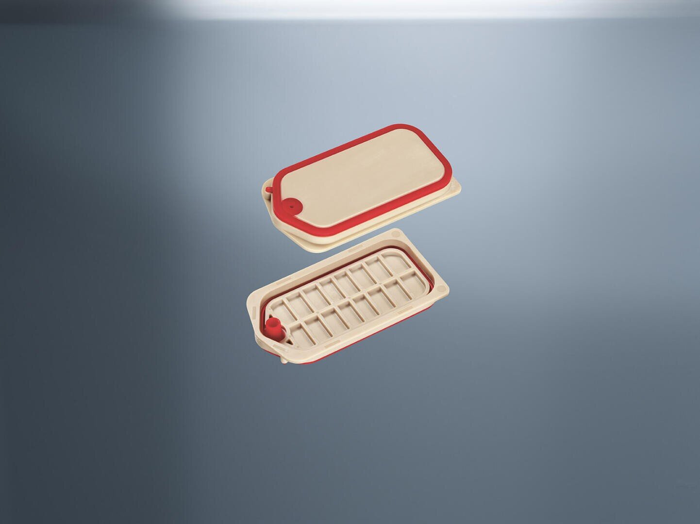 A rectangular, beige and red silicone ice cube tray with a lid, shown open on a smooth blue-gray background. The tray has multiple cube compartments and a matching lid placed beside it.