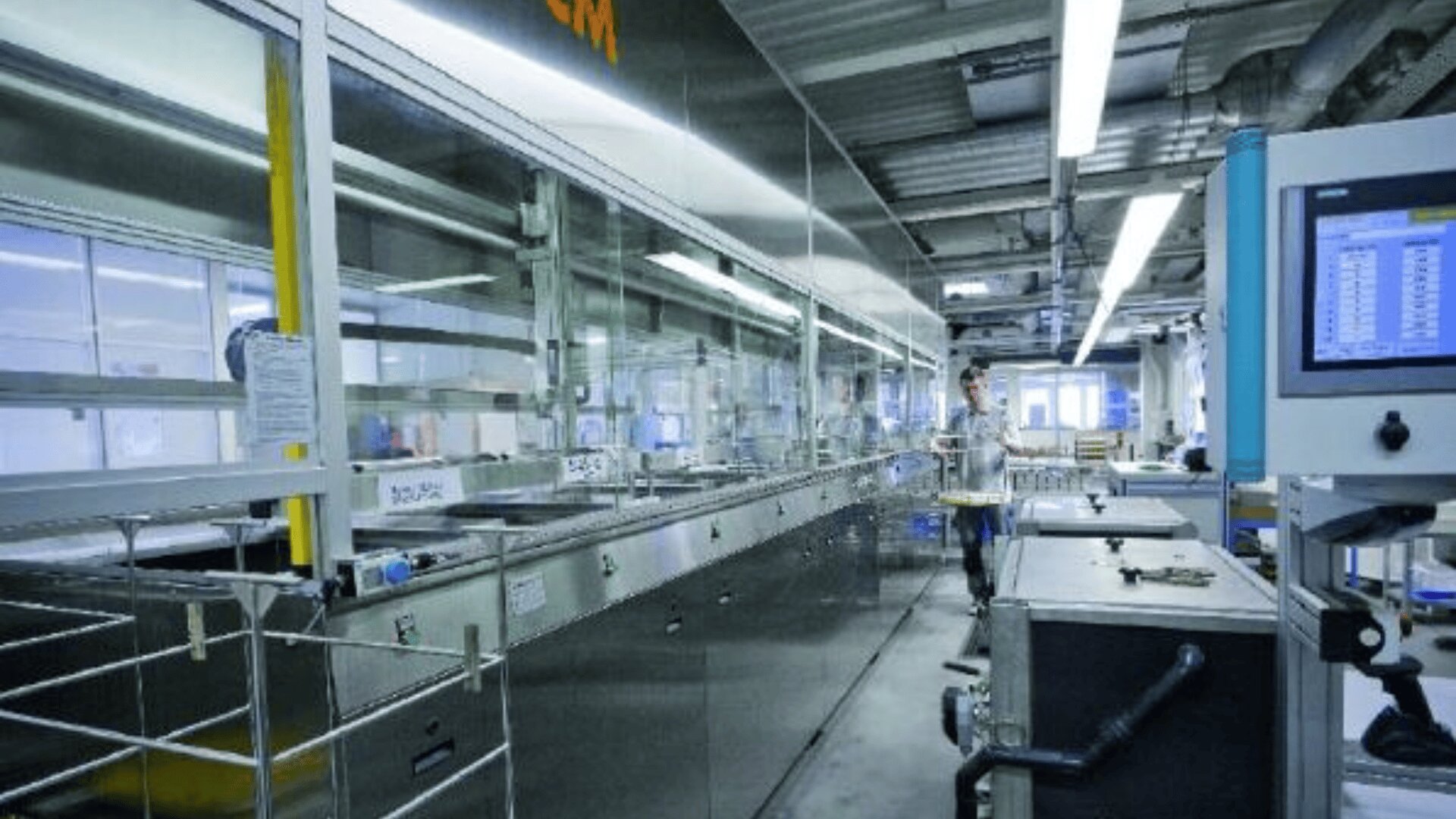 Eine moderne Industrieanlage mit Maschinen aus rostfreiem Stahl, Schalttafeln und Überkopfbeleuchtung. Eine Person steht in der Nähe der Geräte und überwacht den Fertigungsprozess in einer sauberen, organisierten Umgebung.