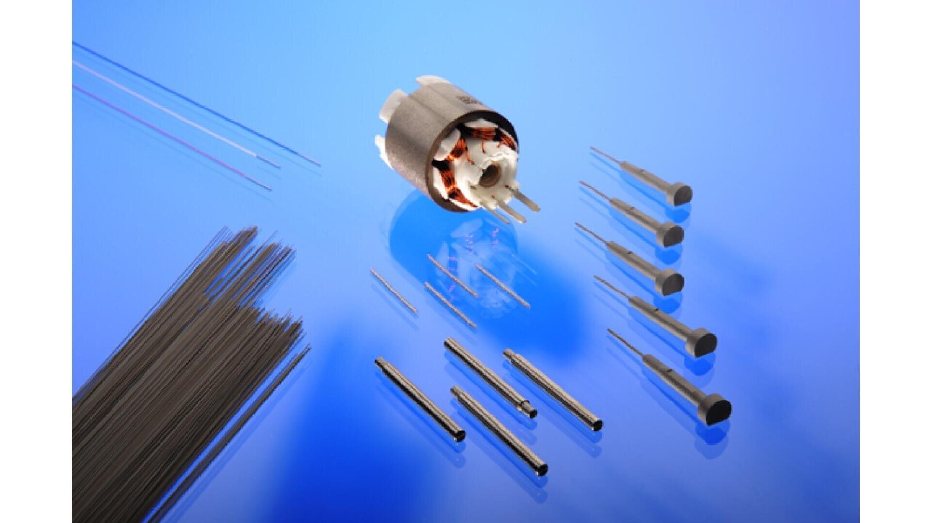 Eine Sammlung kleiner Metallstäbe, Stifte und Präzisionskomponenten, die auf einer blauen Oberfläche angeordnet sind. Nahe der Mitte befindet sich ein zylindrischer mechanischer Teil mit sichtbarer interner Verkabelung.