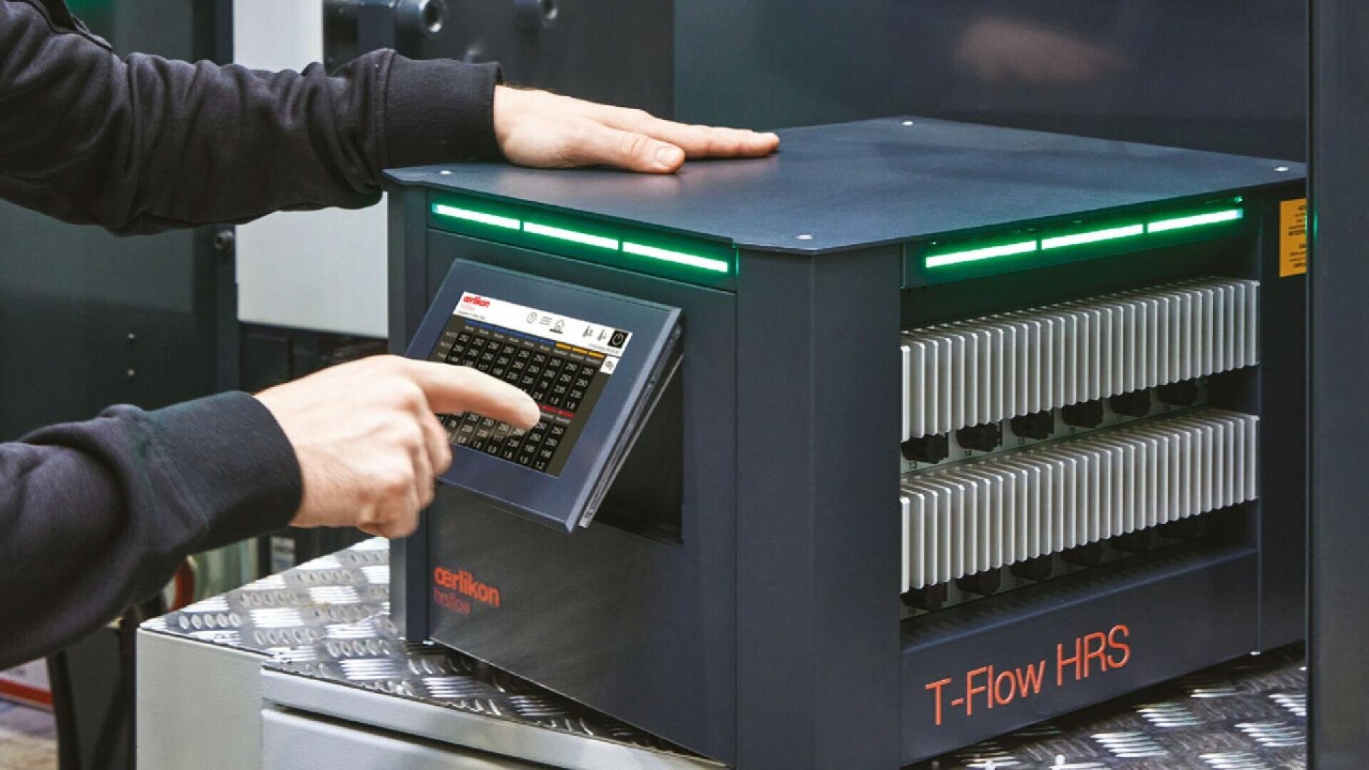 A person operates a T-Flow HRS machine by pressing buttons on its control panel. The device has horizontal vent-like slots and is placed on a metal surface.