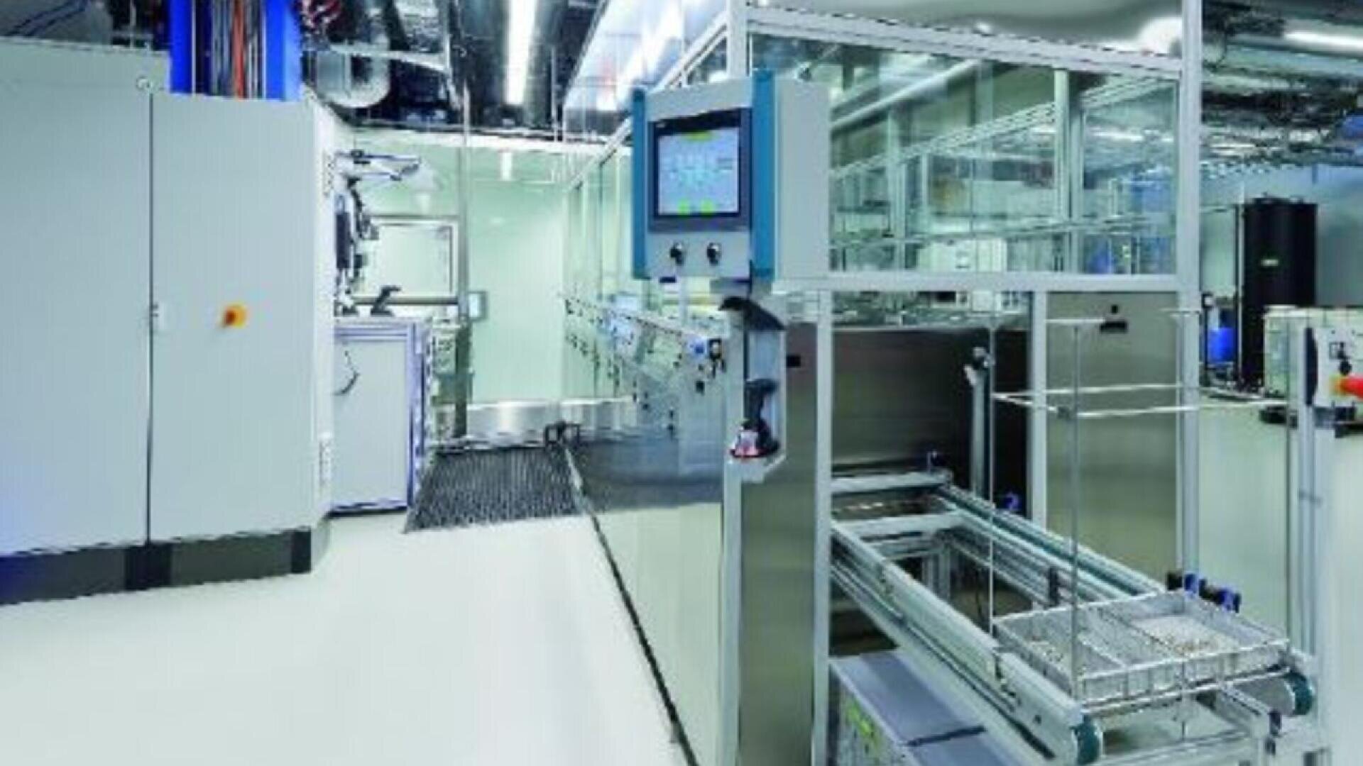 Modern industrial laboratory with stainless steel equipment, conveyor belts, control panels, and glass enclosures, all in a brightly lit, clean environment.