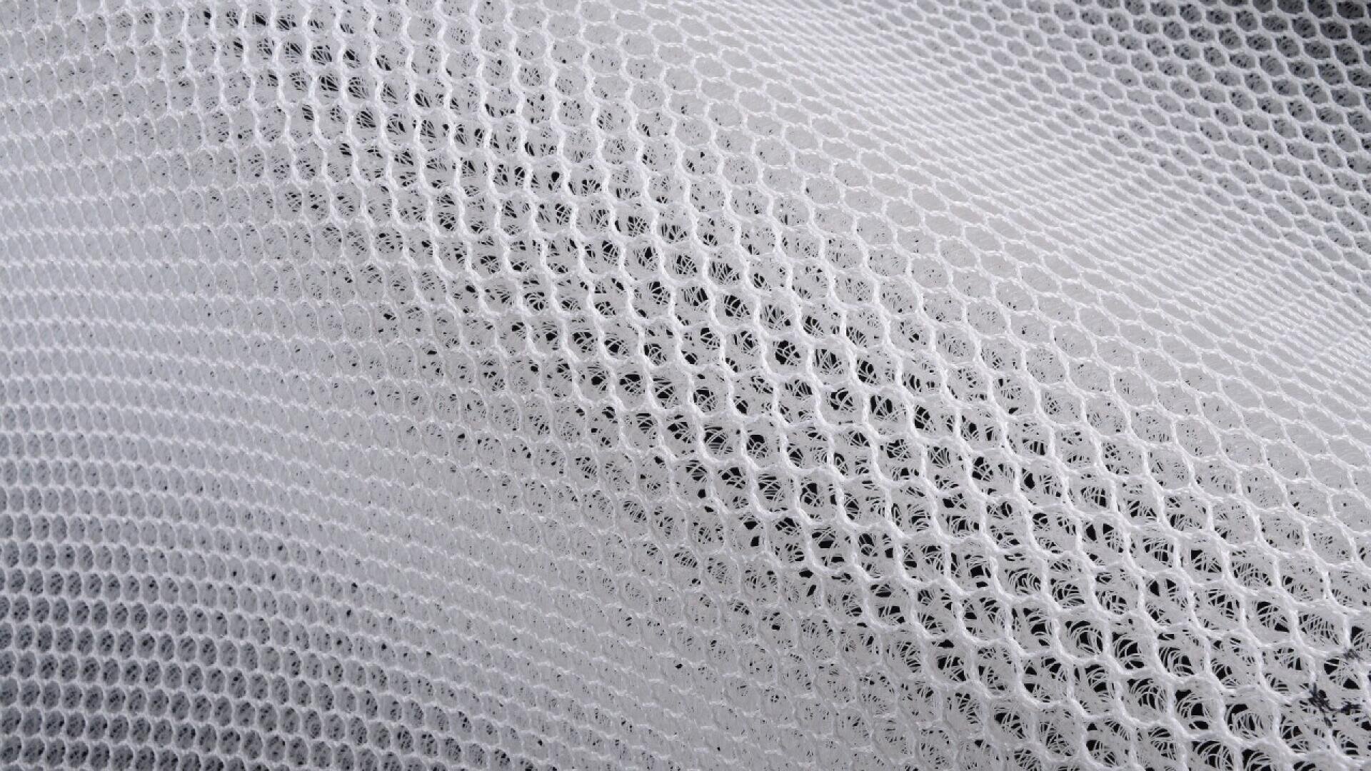 Close-up of a white, mesh fabric with a honeycomb pattern, showing its textured, breathable, and slightly transparent material.