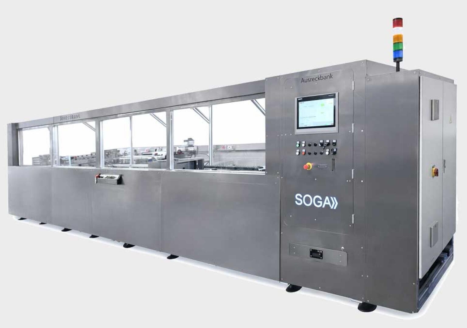 A large industrial machine with a touchscreen control panel, labeled SOGA, featuring buttons, indicator lights, and long side windows revealing internal components. A multi-colored signal light is on top.