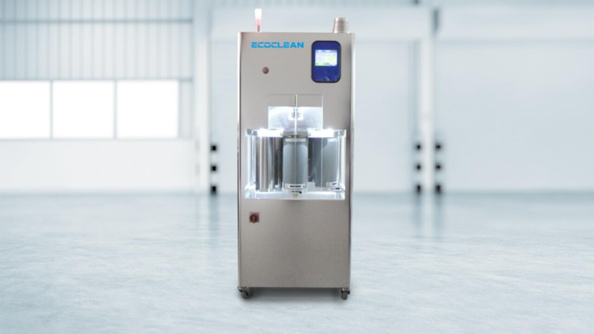 A stainless steel industrial cleaning machine labeled ECOCLEAN stands in a bright, spacious, empty room with large windows and a polished floor.