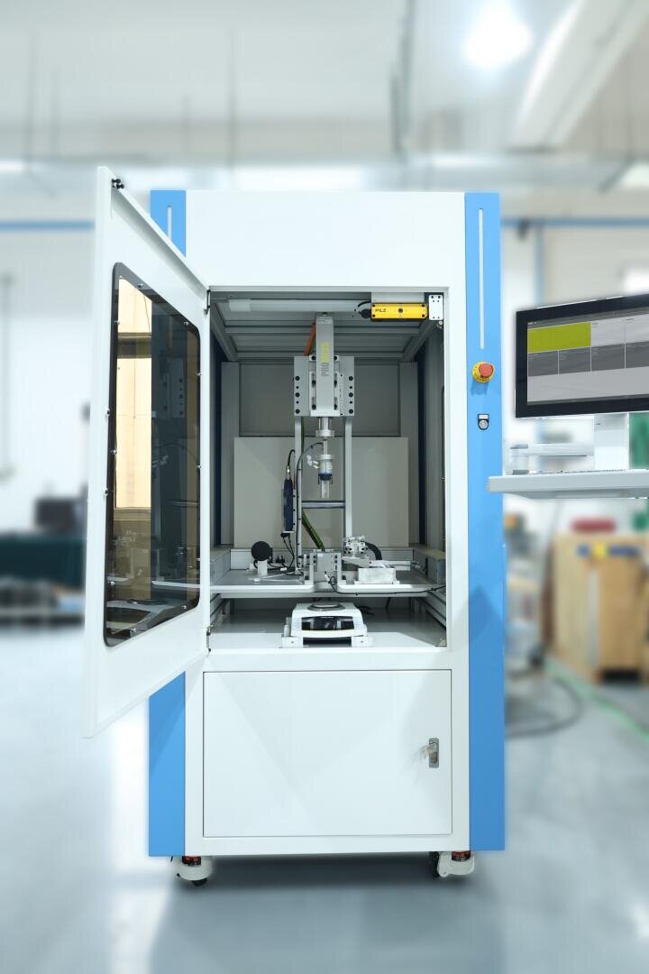 Ein Laborautomat mit offener Tür gibt den Blick auf Roboterarme und Präzisionsinstrumente frei, während rechts ein Computermonitor die Daten anzeigt. Die Umgebung wirkt sauber und industriell.