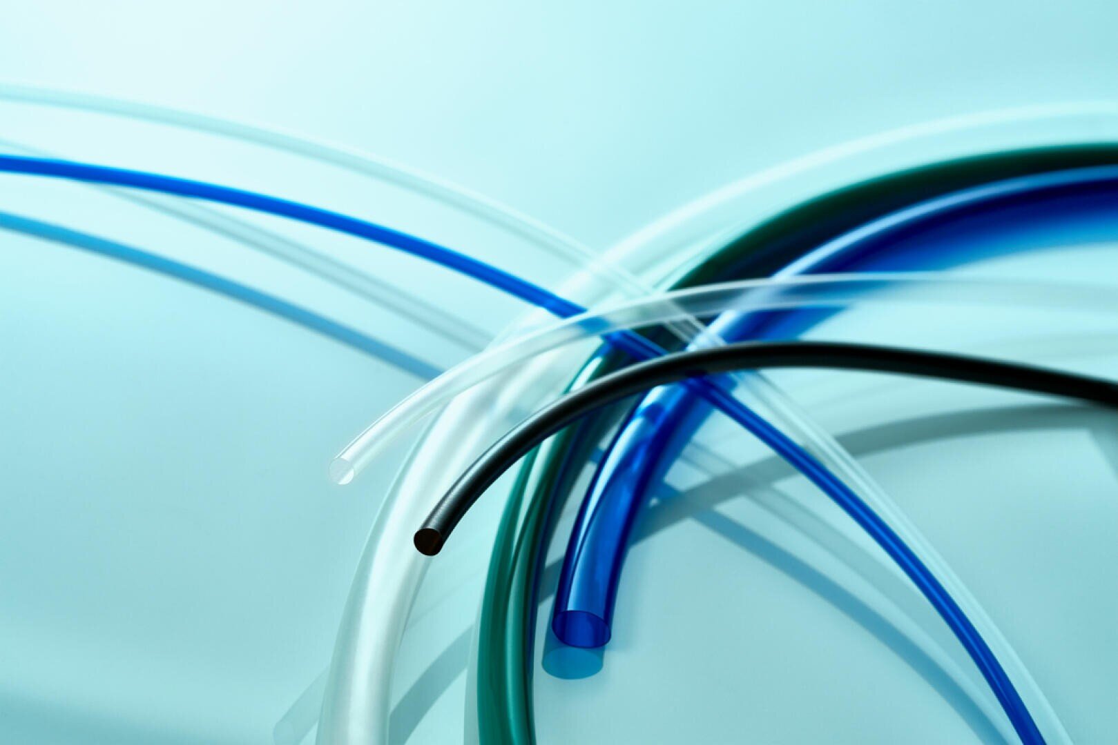 Several colorful plastic tubes, including blue, black, white and clear, are arranged on top of each other on a light blue background. The lighting creates soft reflections and a clean, modern look.