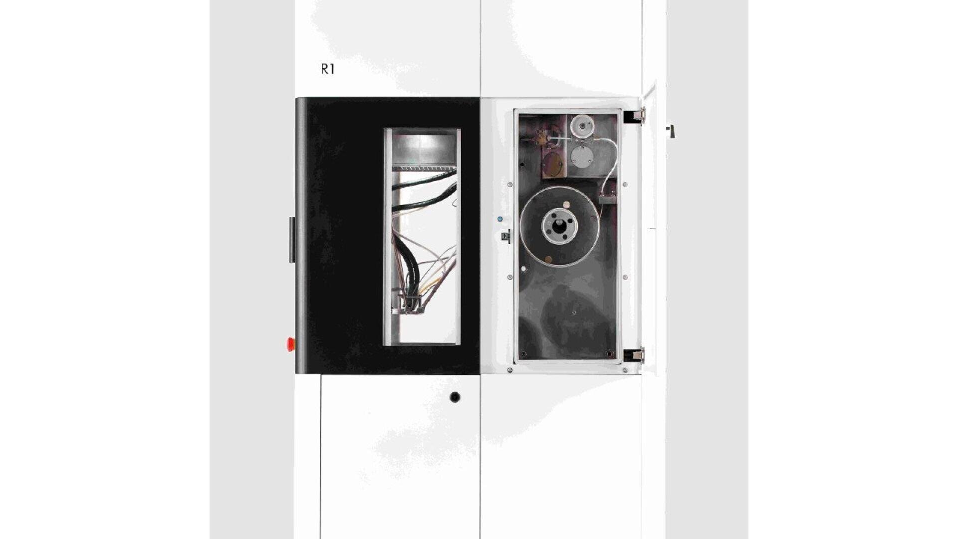Front view of a white industrial machine with a black-framed window on the left showing wiring and components, and a transparent panel on the right revealing internal mechanical parts and gears.