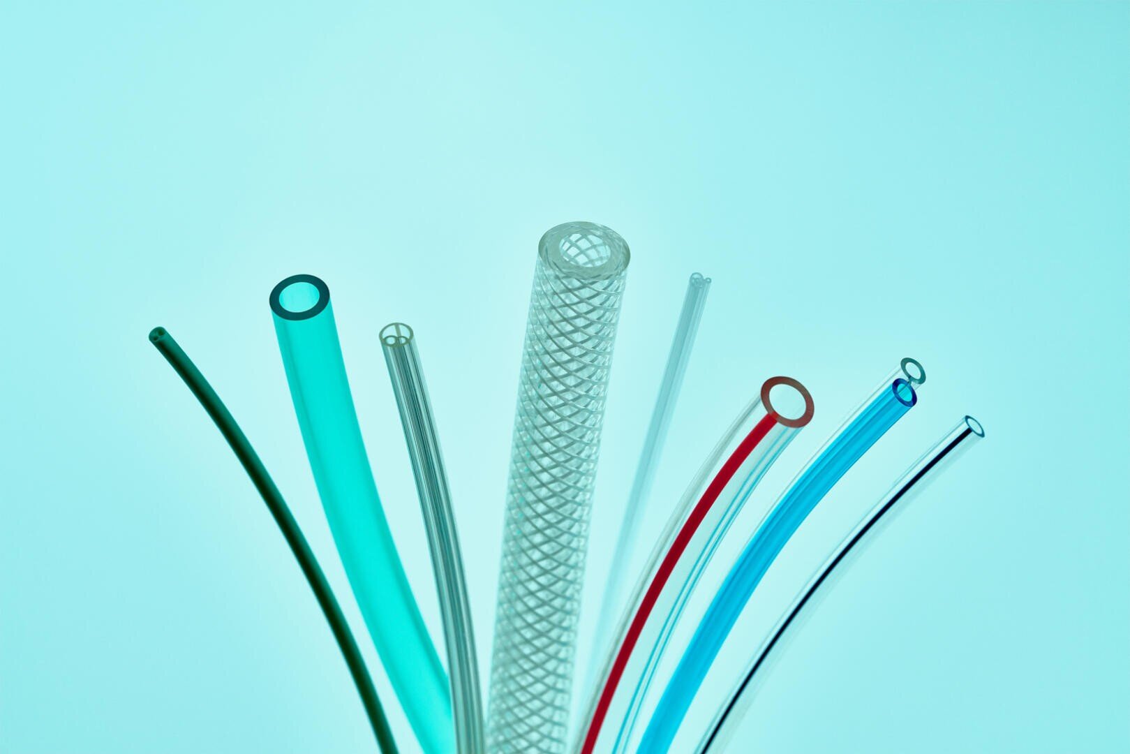 A variety of plastic and rubber tubes in different colors and thicknesses are arranged in a fan shape against a light blue background.