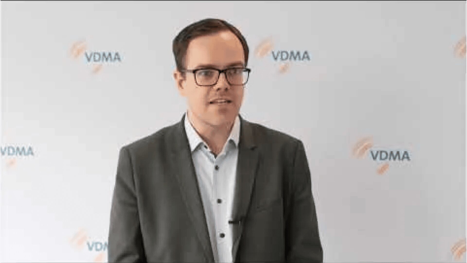 Ein Mann mit Brille und grauem Sakko steht vor einer Kulisse mit dem VDMA-Logo, blickt leicht zur Seite und spricht.