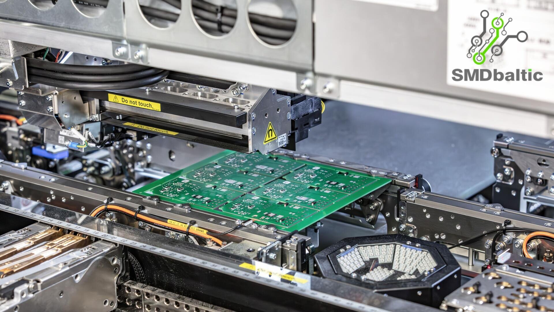 Nahaufnahme einer Maschine, die grüne Leiterplatten (PCBs) in einer Elektronikfertigungsanlage zusammensetzt, mit dem SMD Baltic-Logo in der oberen rechten Ecke.