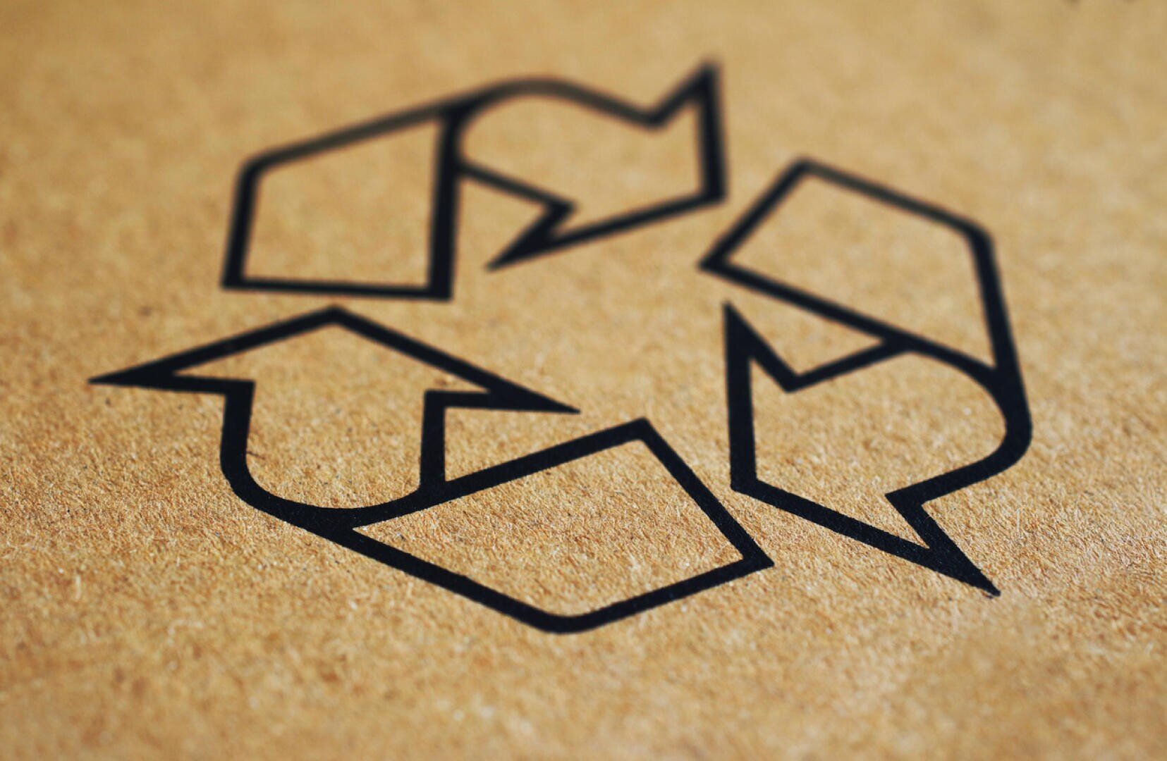 Close-up of a black recycling symbol with three arrows forming a triangle, printed on brown cardboard.