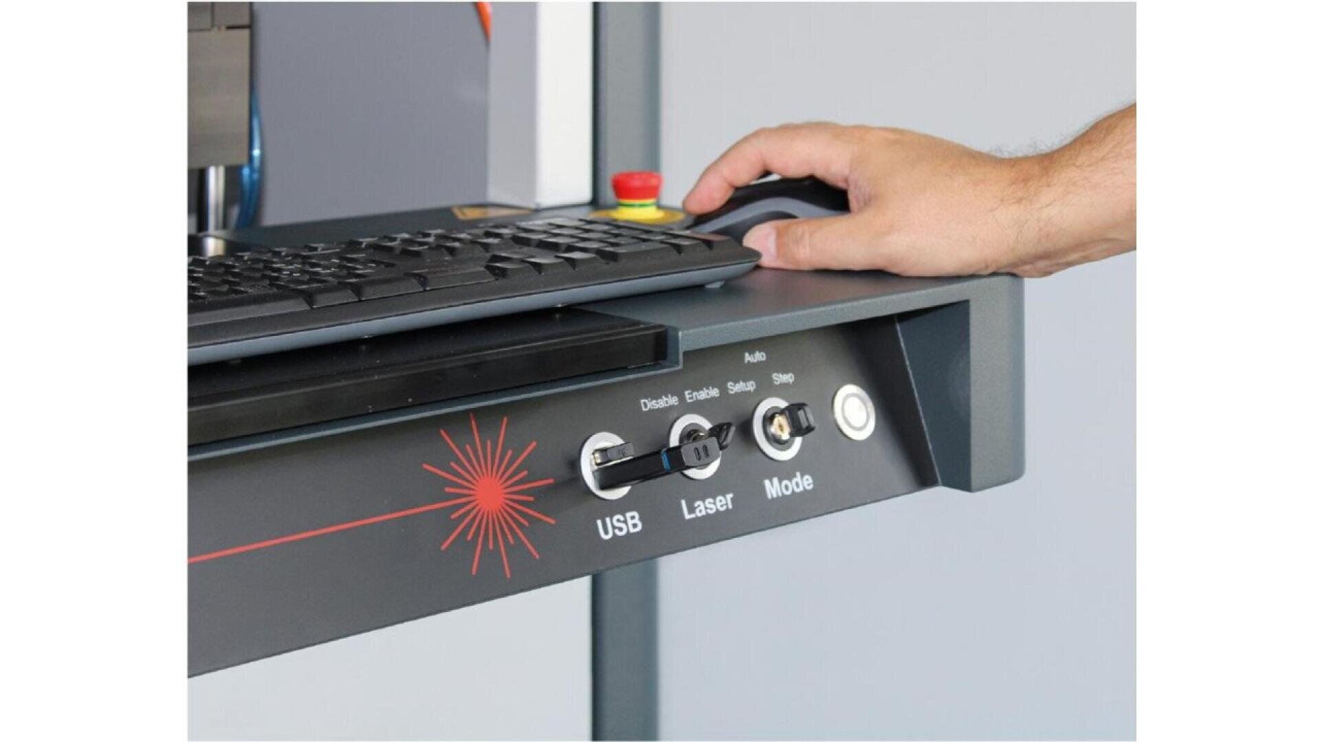 A person’s hand uses a mouse next to a keyboard on a control panel with switches labeled USB, Laser, and Mode, along with a red emergency stop button and a red laser symbol.