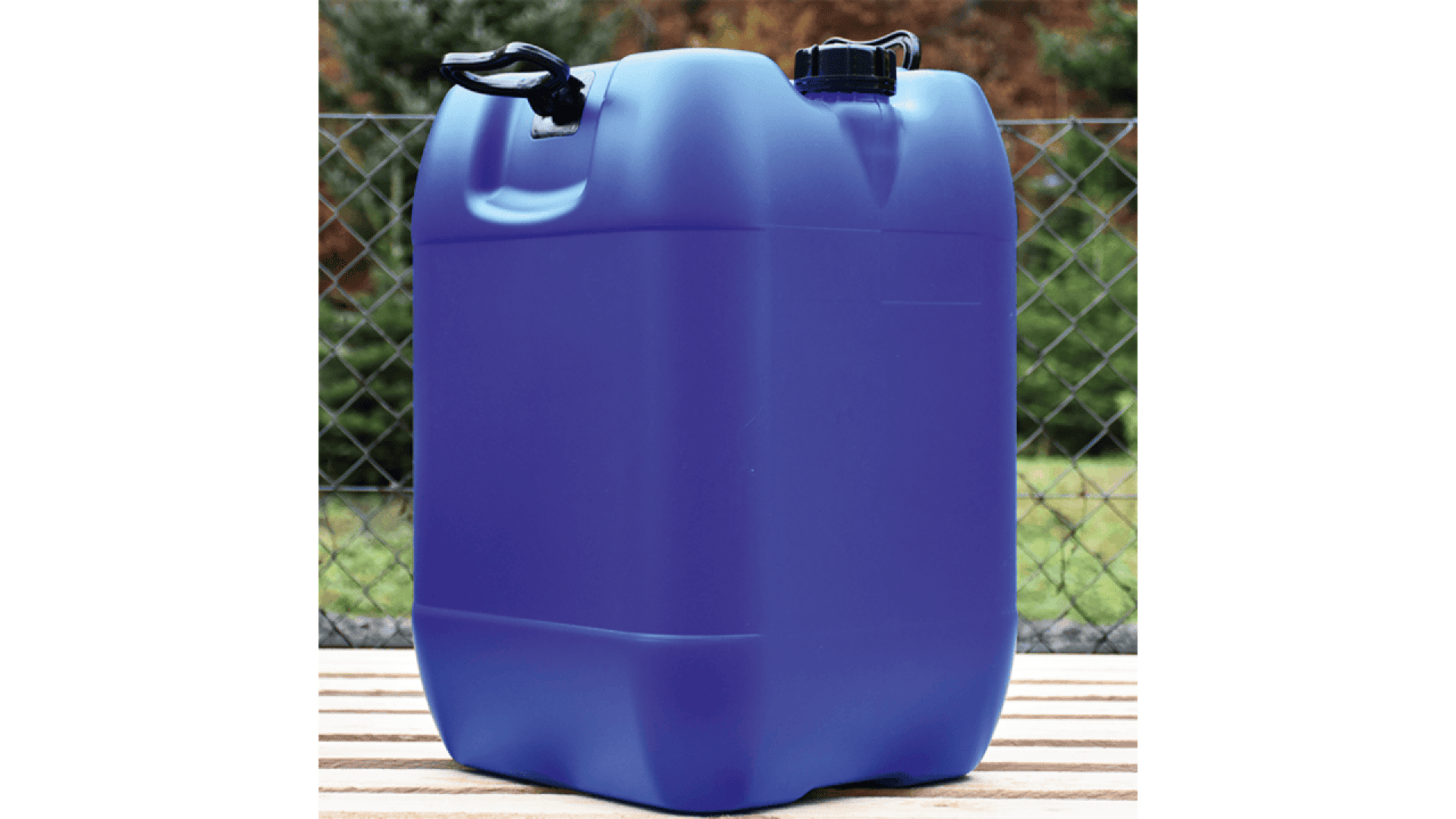 A large blue plastic jerry can with a black cap and handle sits on a wooden surface outdoors, in front of a chain-link fence and greenery.