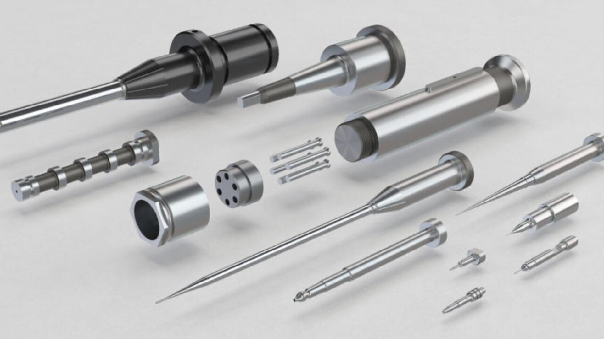 A set of precision-engineered metal components, including cylindrical parts, rods, and needle-like instruments, arranged neatly on a light gray surface.