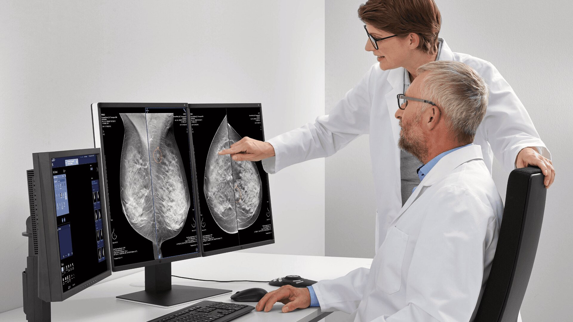 Zwei Medizinerinnen in weißen Kitteln untersuchen Röntgenaufnahmen der Brust, die auf zwei Computermonitoren angezeigt werden. Eine zeigt auf den Bildschirm, die andere schaut aufmerksam zu und bespricht die Bilder in klinischer Umgebung.