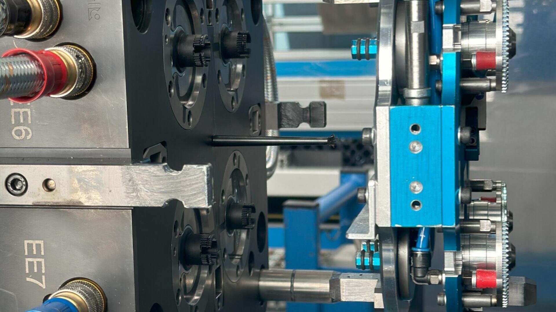Close-up of an industrial injection molding machine with metal plates, gears, and blue mechanical components, showing detailed parts and connections in a manufacturing setting.