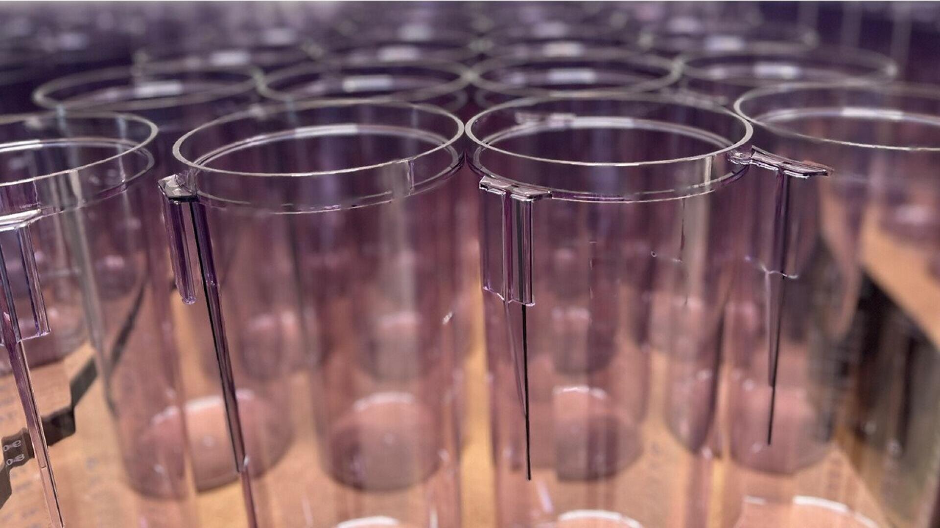 A close-up view of several transparent, cylindrical plastic containers arranged in rows on a flat surface, with a soft purple tint and reflective highlights.
