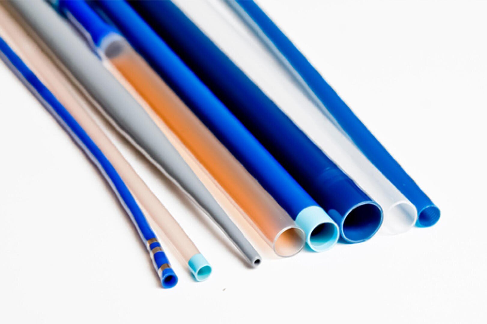 A group of different medical catheters in various colors and sizes is arranged next to each other on a white background.
