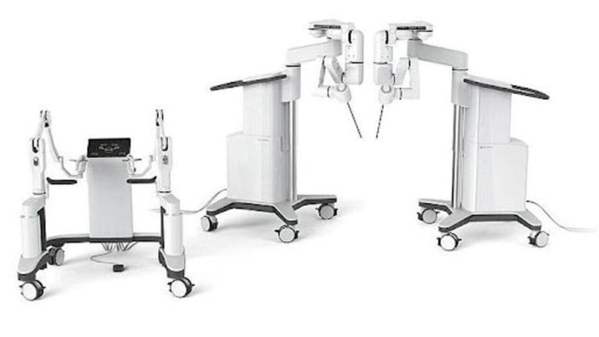 Two white robotic surgical systems with multiple articulated arms and wheeled bases are shown on a plain background, designed for precise minimally invasive medical procedures.