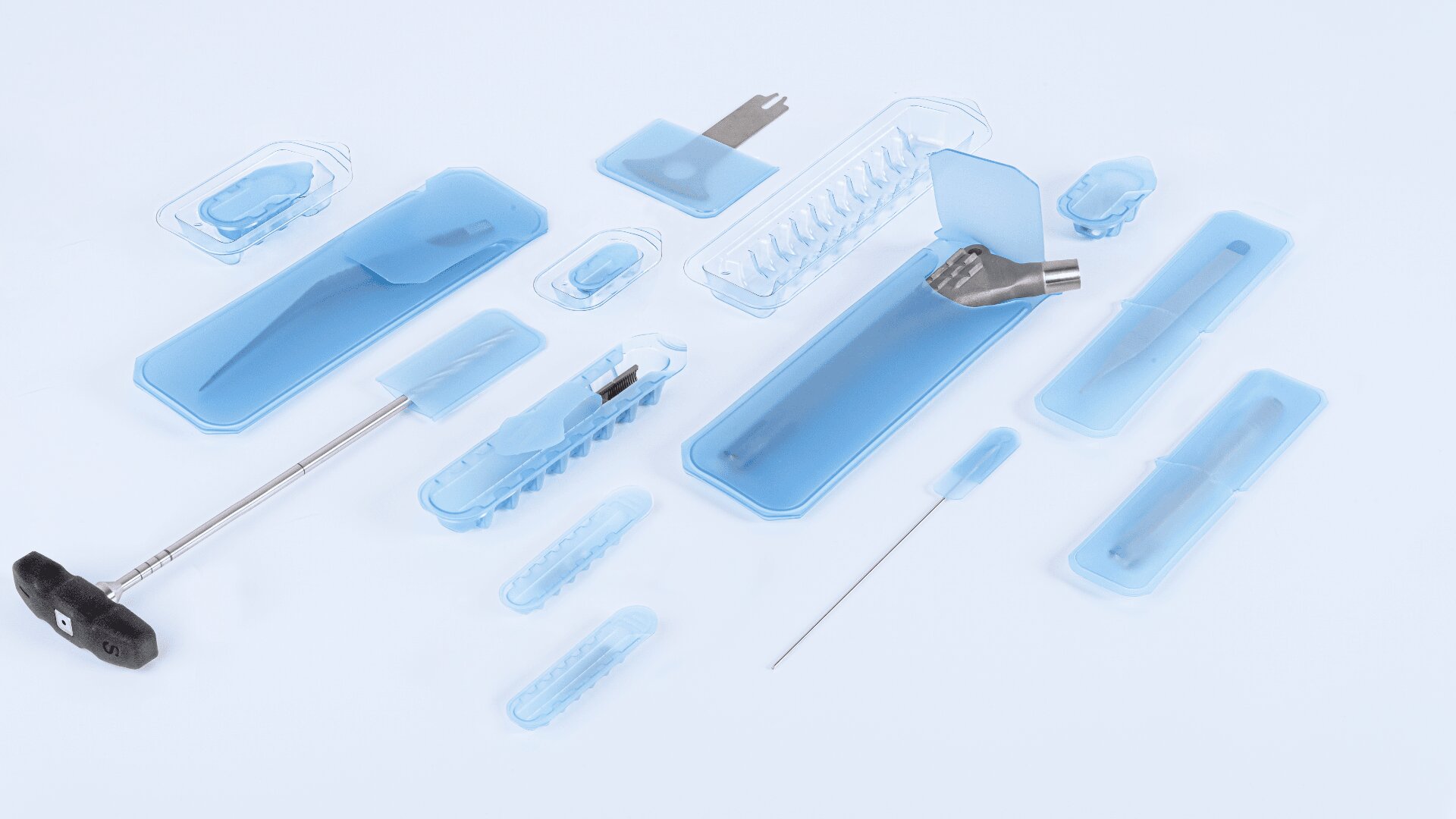 Assorted medical instruments and tools in blue sterile packaging are arranged neatly on a white surface.