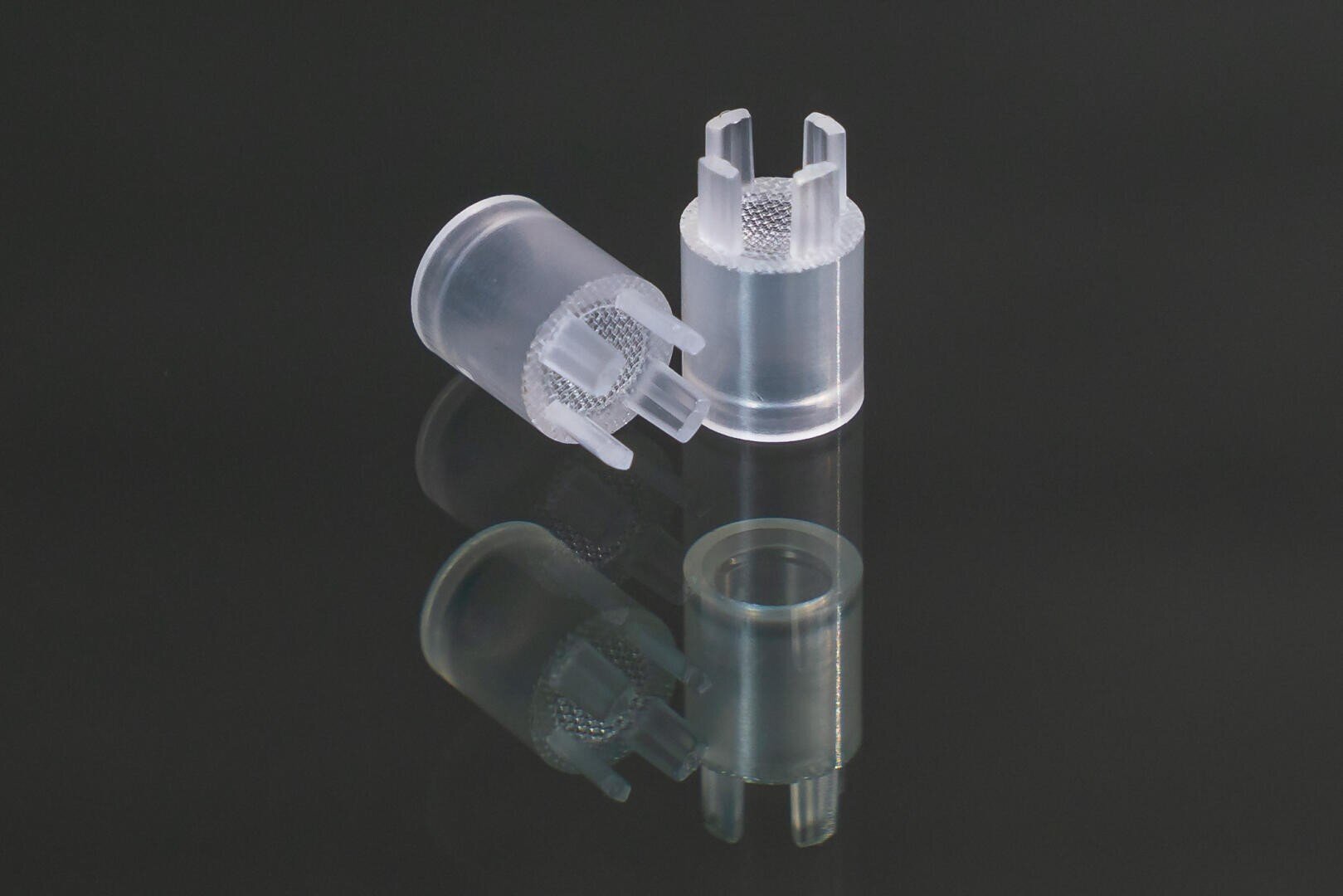 Zwei zylindrische Komponenten aus klarem Kunststoff mit strukturierten Griffen und offenen Zinken sind auf einer glänzend schwarzen Oberfläche platziert, wodurch eine Reflexion entsteht.