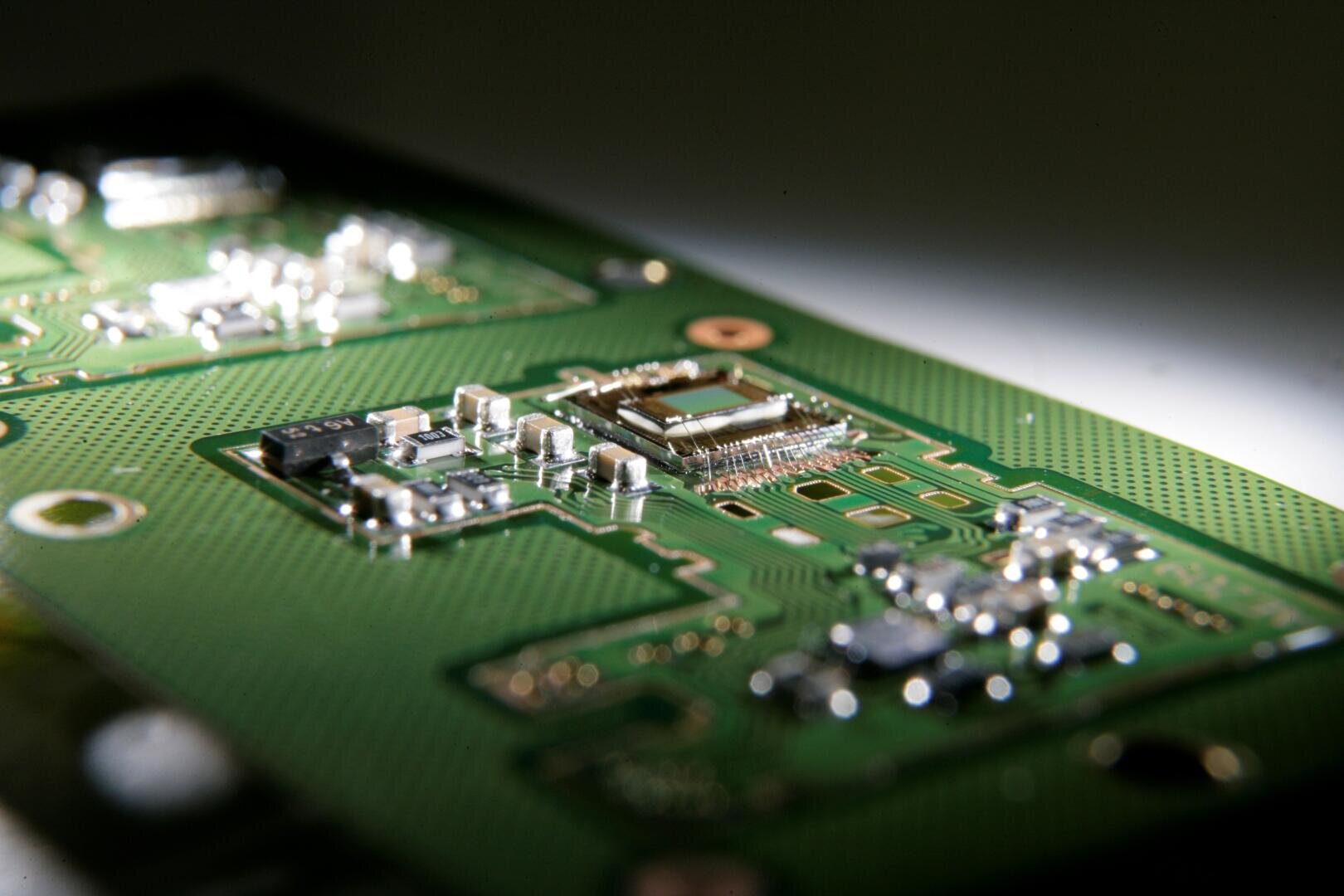 Close-up of an electronic circuit board with various components, such as microchips and resistors, mounted on a green printed circuit board, lit with focused lighting.