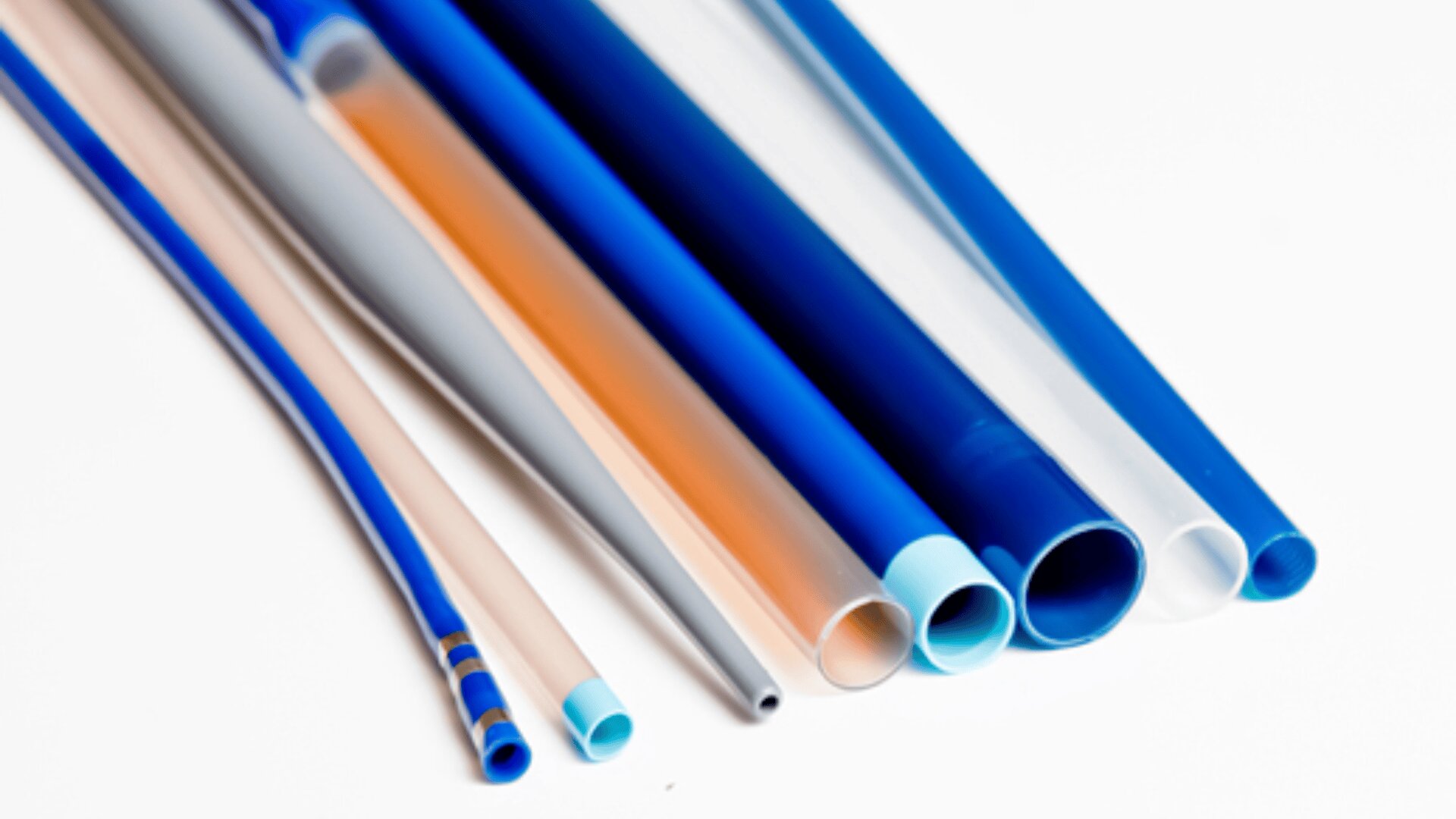 Verschiedene bunte Kunststoff- und Silikonschläuche, meist blau, weiß und orange, sind nebeneinander auf einer weißen Fläche angeordnet. Die Schläuche unterscheiden sich in Durchmesser, Dicke und Transparenz.
