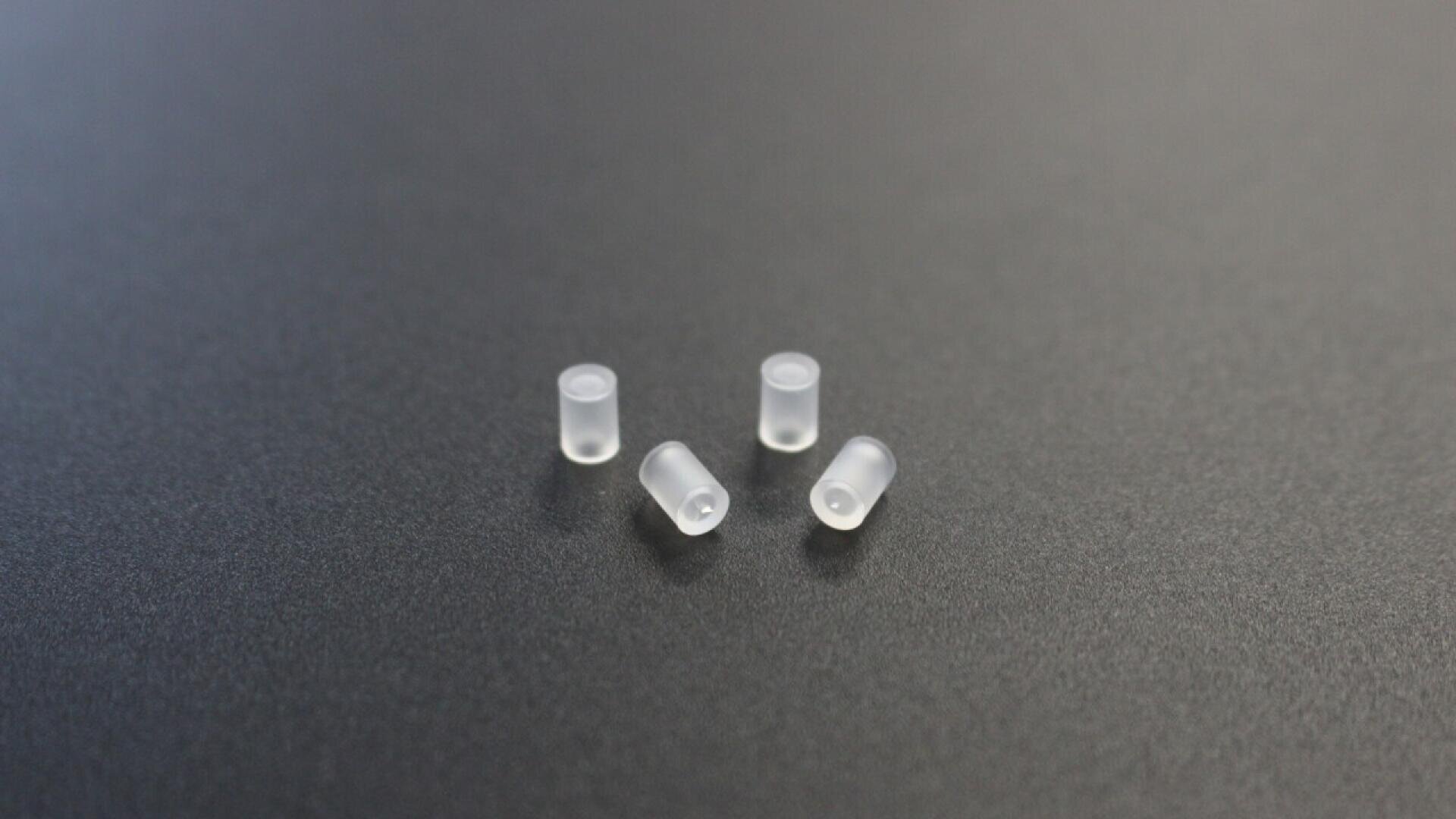 Four small, translucent plastic cylindrical caps are placed on a smooth, dark gray surface.