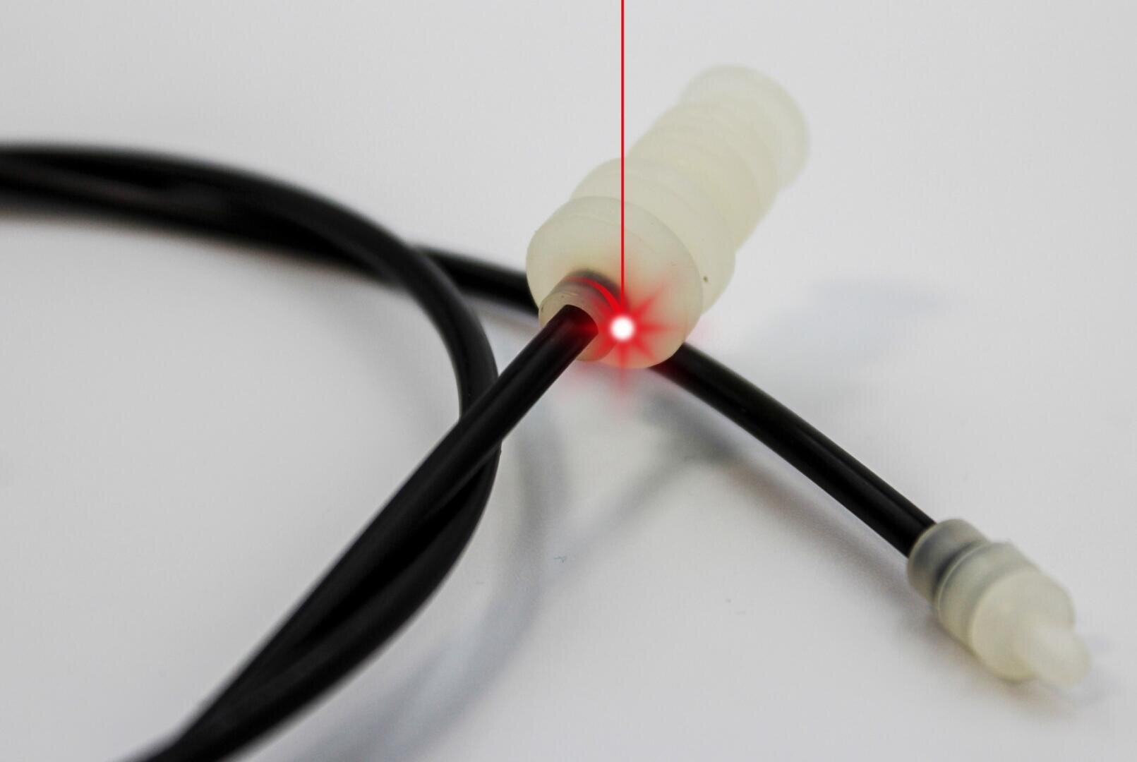 Nahaufnahme eines schwarzen Glasfaserkabels, das von seinem Stecker ein rotes Laserlicht ausstrahlt, wobei das Kabel aufgerollt und ein weiterer Stecker im Hintergrund sichtbar ist.