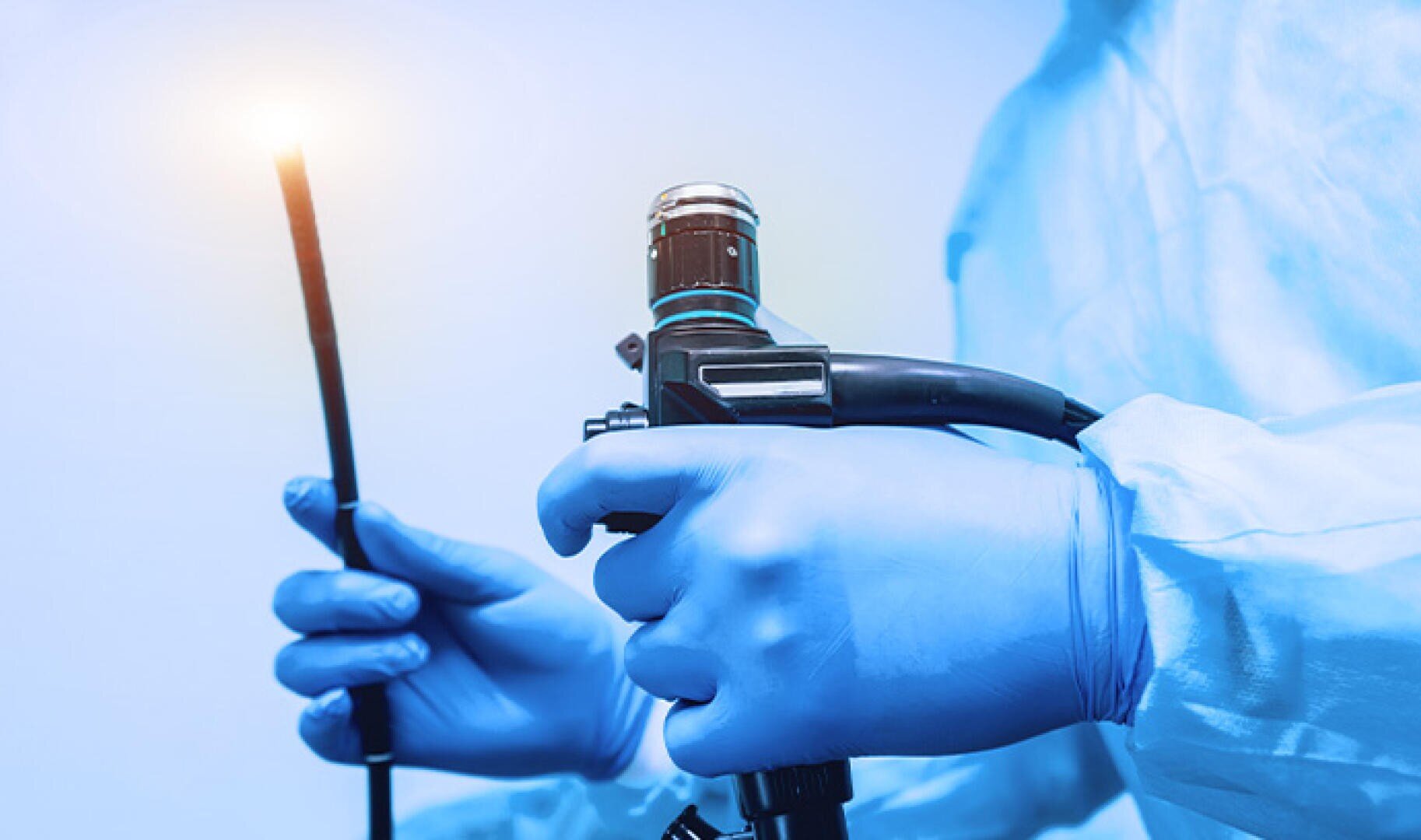 Eine Person, die blaue medizinische Handschuhe und einen Kittel trägt, hält ein Endoskop, ein flexibles medizinisches Instrument mit einer Lichtquelle an der Spitze, das für innere Untersuchungen verwendet wird.