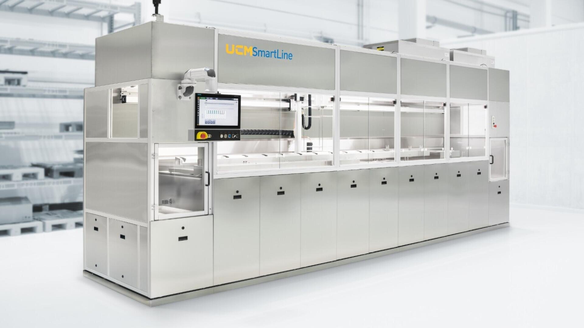 A large, stainless steel industrial cleaning machine labeled UCM SmartLine with a touchscreen control panel, set in a bright, modern factory environment.
