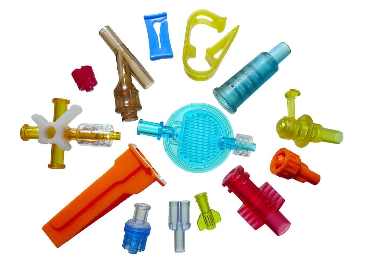Assorted colorful plastic medical connectors and parts arranged in a circular pattern on a white background.