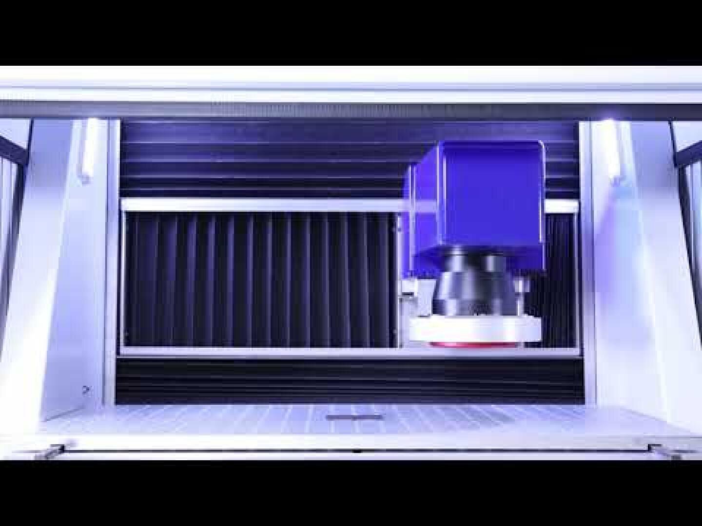 A close-up of a laser engraving or cutting machine in operation, showing the laser head above a metal work surface inside the machine.