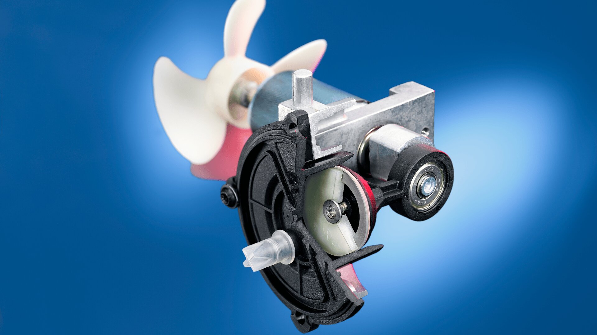 Ein mechanisches Gerät mit freiliegendem Querschnitt zeigt vor einem blauen Hintergrund mit Farbverlauf interne Zahnräder und einen kleinen Propeller.