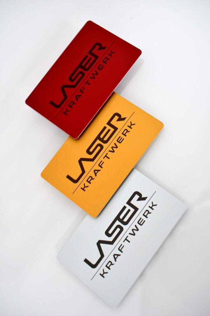 Drei rechteckige Karten in Rot, Gelb und Silber sind diagonal auf einem weißen Hintergrund gestapelt. Auf jeder Karte steht der Text LASER KRAFTWERK in fetten Großbuchstaben.