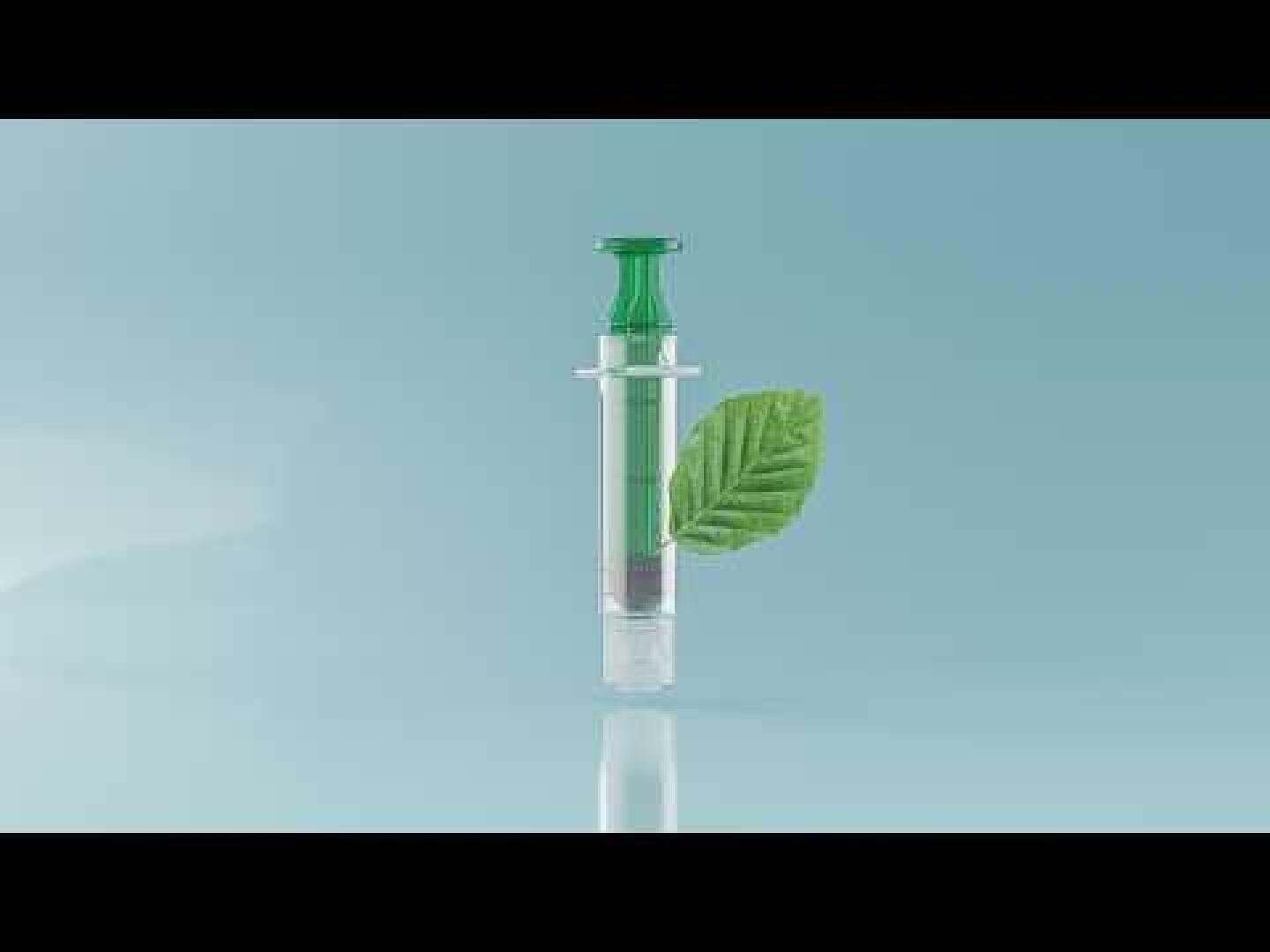 A syringe filled with a green liquid stands upright against a light blue background. A green leaf is attached to its side, symbolizing environmentally friendly or natural medicine.