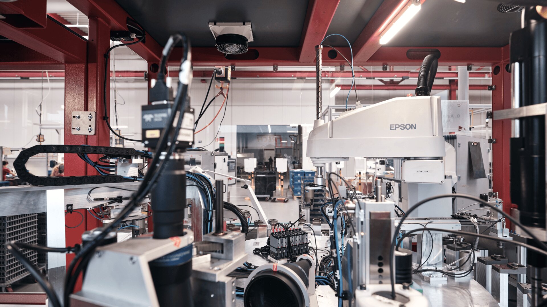 Eine moderne industrielle Fertigungsanlage mit Roboterarmen, Maschinen und Kabeln, einschließlich einer Epson-Robotereinheit, die an automatisierten Montagelinien in einer hell erleuchteten Fabrikumgebung arbeiten.