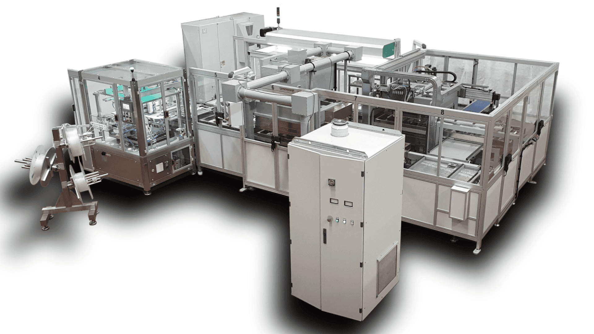 A large, automated industrial machine for manufacturing or packaging, featuring multiple enclosed components, control panels, conveyor belts, and a reel dispenser on the left side. The setup is clean and metallic.