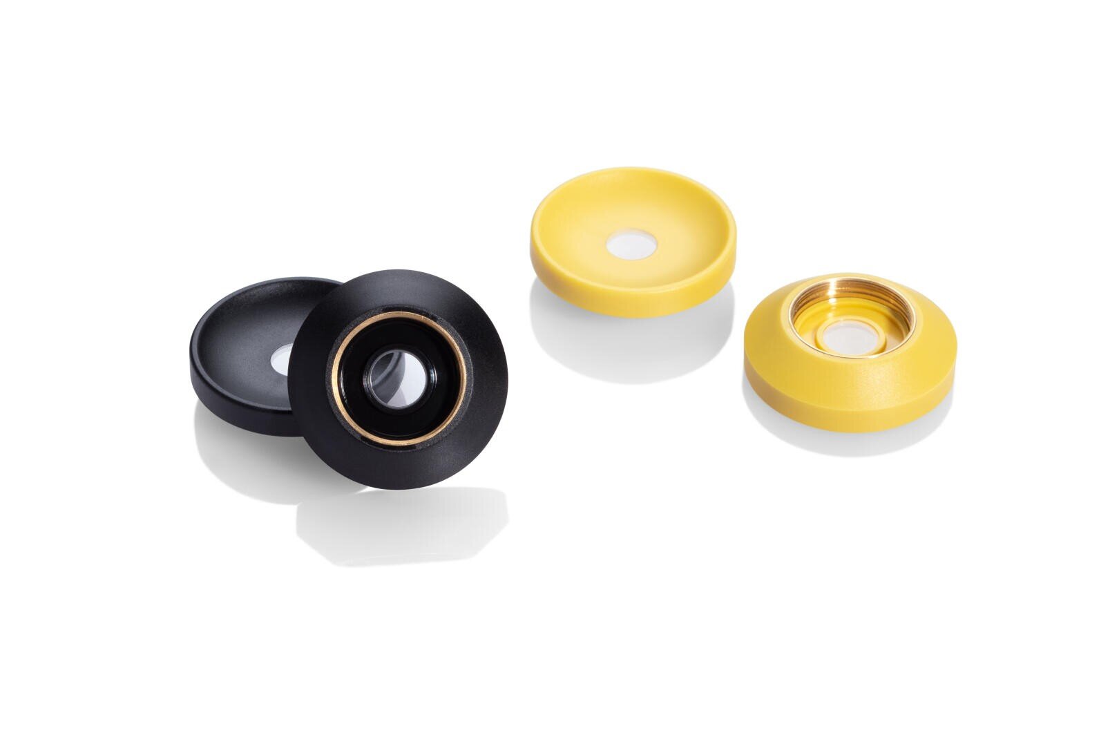 Vier kreisförmige Objekte, zwei schwarze und zwei gelbe, jeweils mit einem metallischen Ring oder Zentrum, sind auf einem weißen Hintergrund angeordnet. Die Objekte scheinen kleine mechanische oder elektronische Komponenten zu sein.