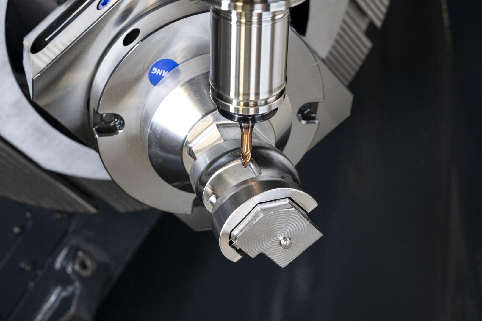Eine CNC-Maschine fräst präzise ein komplexes Metallteil mit einem an einer Spindel befestigten rotierenden Schneidwerkzeug. Das Teil und das Werkzeug sind auf speziellen Vorrichtungen montiert.