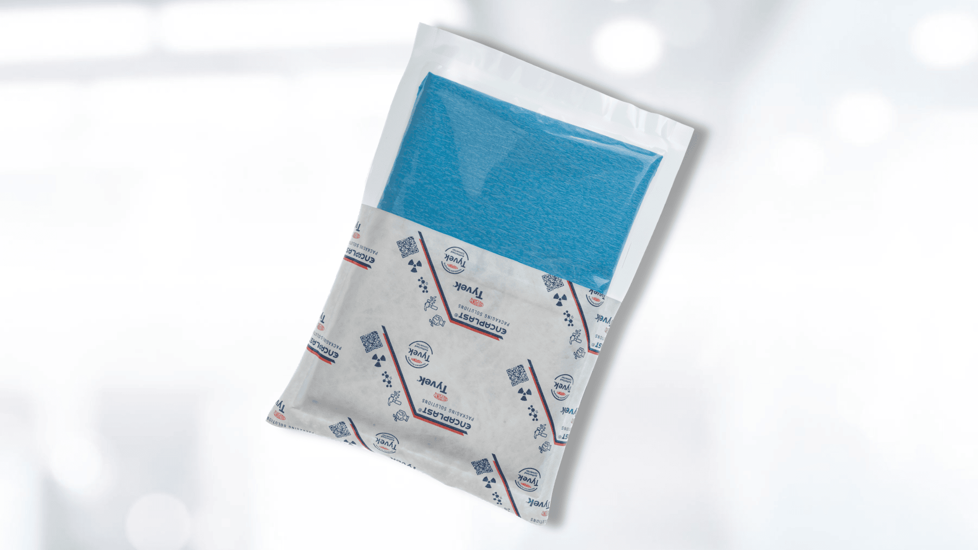 Ein versiegeltes Paket, das ein gefaltetes blaues Tuch enthält, das teilweise über einer weißen Hülle sichtbar ist, die mit blauem und rotem Text und Symbolen vor einem verschwommenen hellen Hintergrund bedruckt ist.