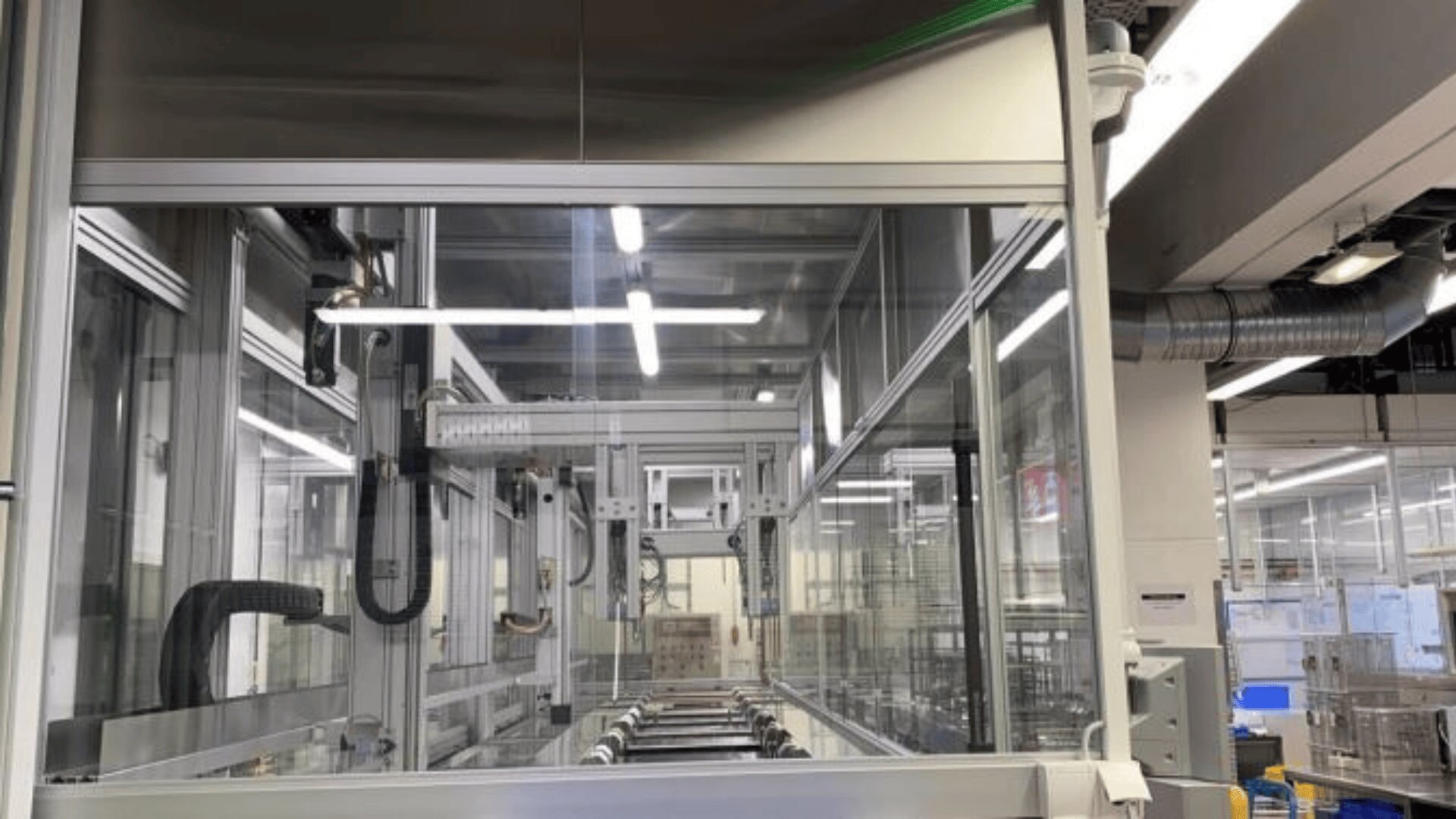 Automatisierte Maschinen in einer hellen, modernen Fabrik mit Glaswänden, Oberlichtern, Metallrohren und verschiedenen mechanischen Komponenten.