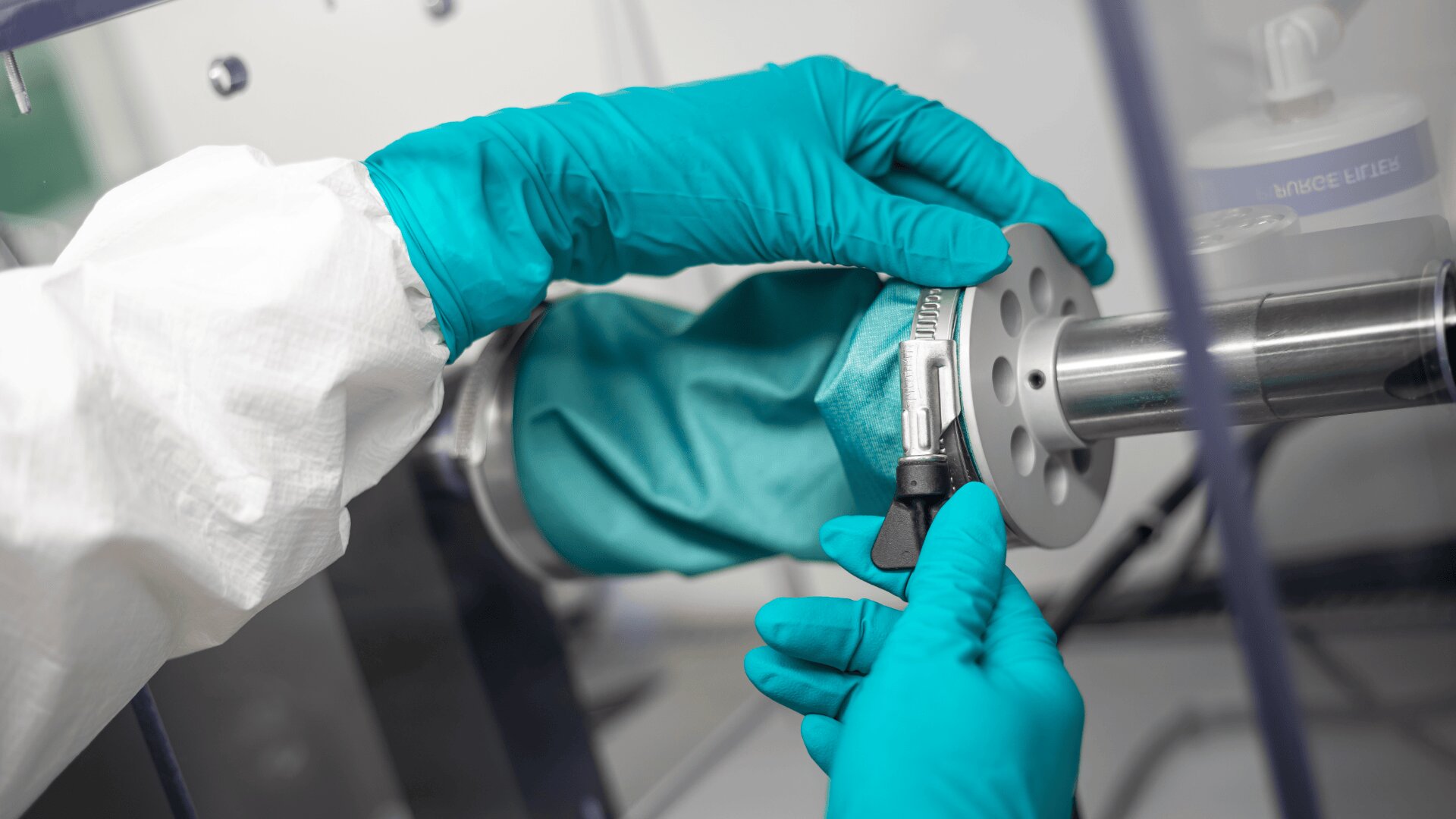 Eine Person mit Schutzhandschuhen und Laborkittel führt ein Probengefäß in einen Anschluss an einem wissenschaftlichen Gerät in einem Labor ein.