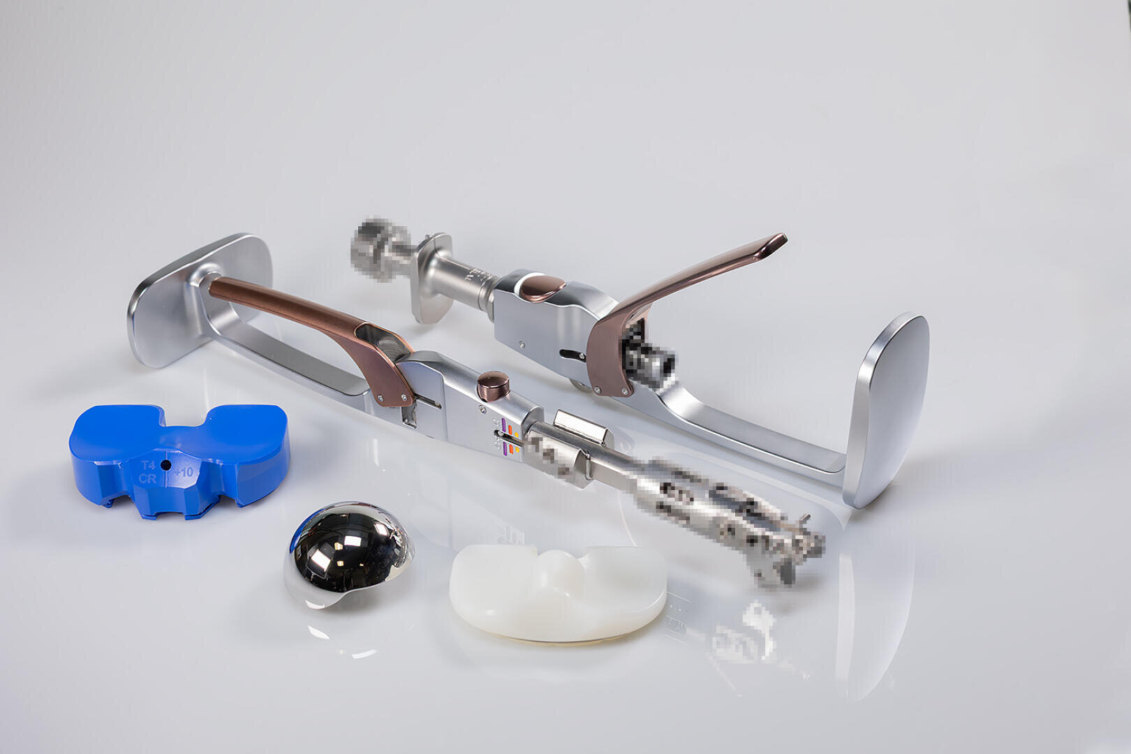 A set of orthopaedic surgical instruments and implants, including a metallic device, a blue plastic mold, a shiny metal ball and a white plastic component arranged on a white surface.
