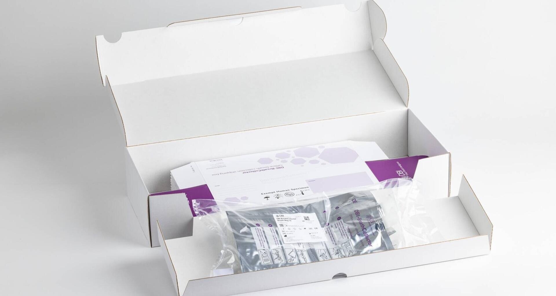 Eine weiße Pappschachtel ist geöffnet und gibt den Blick frei auf einen versiegelten, durchsichtigen Plastikbeutel mit einem Etikett, einer lilafarbenen Anleitung und Papierkram im Inneren, alles fein säuberlich vor einem weißen Hintergrund angeordnet.