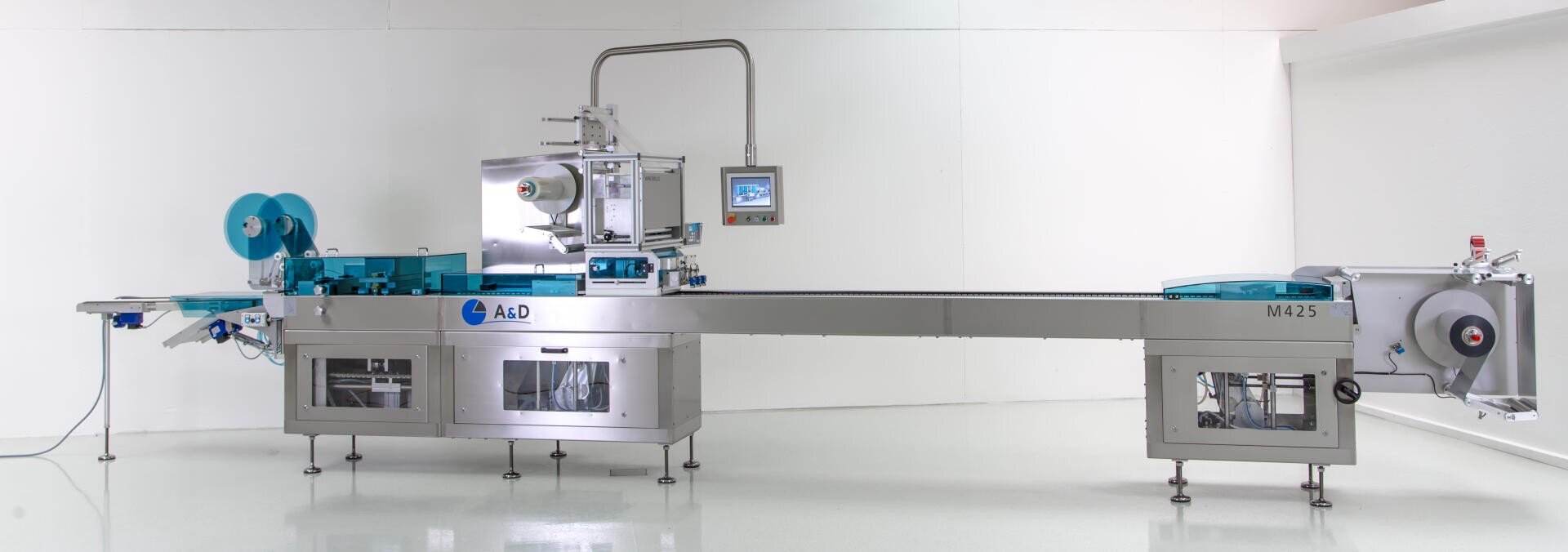 Eine große, moderne automatisierte Verpackungsmaschine mit Edelstahlteilen, blauen Akzenten, Kontrollbildschirmen und Förderbändern, aufgestellt in einem sauberen, weißen Industrieraum.