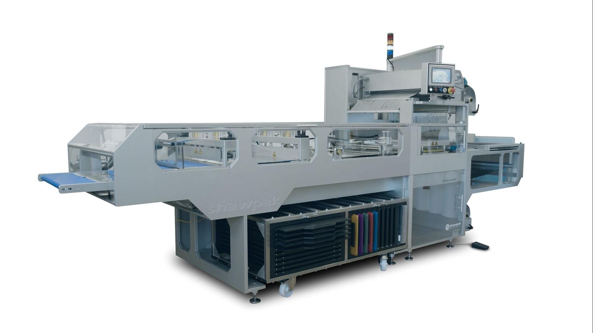 Eine große industrielle Verpackungsmaschine aus Edelstahl mit einem Förderband, einem Bedienfeld und darunter liegenden Regalen, die für die automatische Verpackung von Lebensmitteln oder Produkten konzipiert ist.