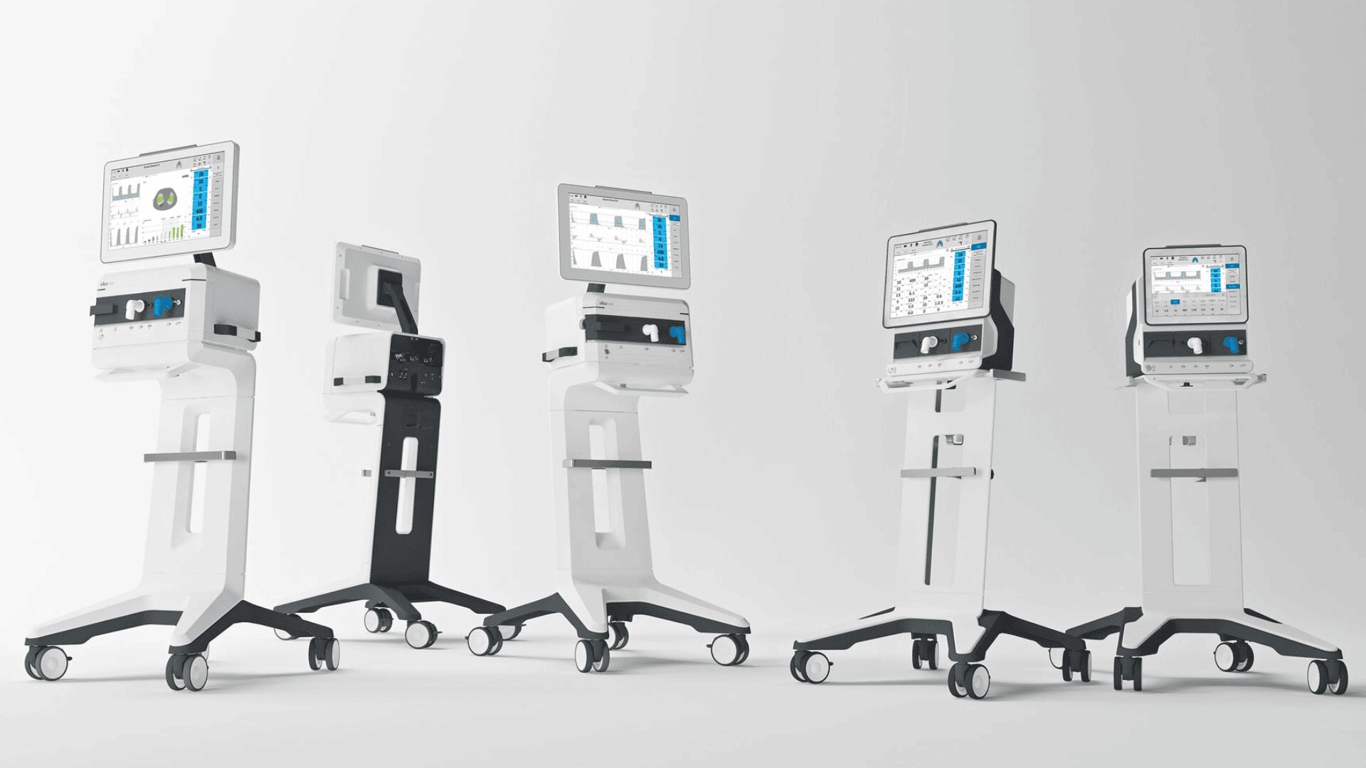 Fünf moderne medizinische Beatmungsgeräte mit digitalen Bildschirmen sind in einer Reihe auf fahrbaren Ständern vor einem schlichten weißen Hintergrund aufgestellt. Die Bildschirme zeigen Diagramme und Daten zur Patientenüberwachung.